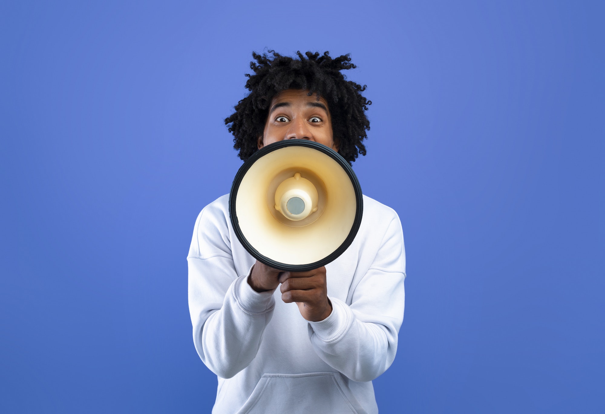 Emotional black teenager making announcement with megaphone on blue studio background